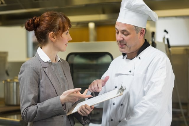 Young female manager talking to the head cook standing in a professional kitchen.jpeg